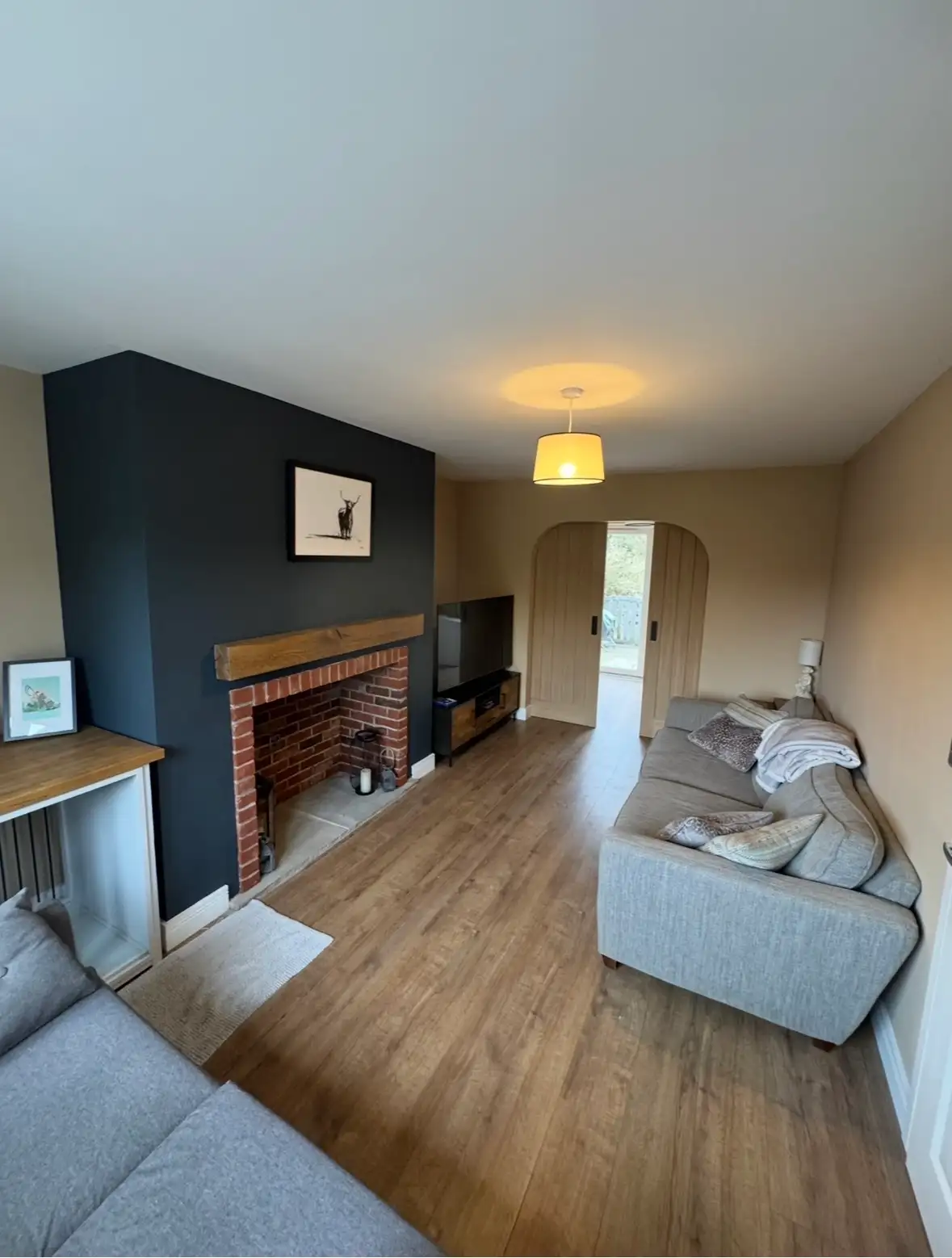 Finished living room with laminate floor, brick-slip chimney breast and oak mantle