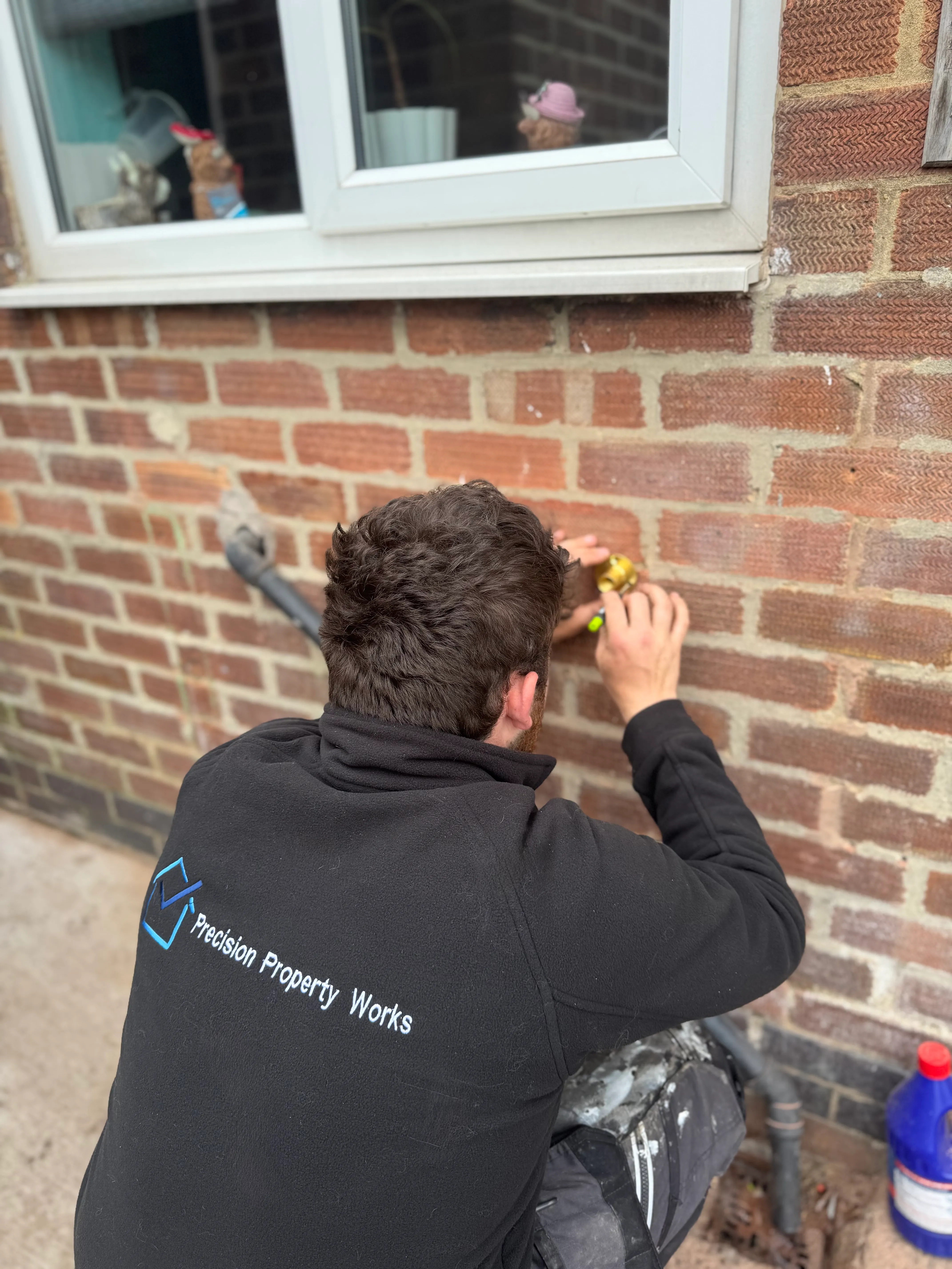 Tradesman in a Precision Property Works fleece fitting an outside tap to a brick wall