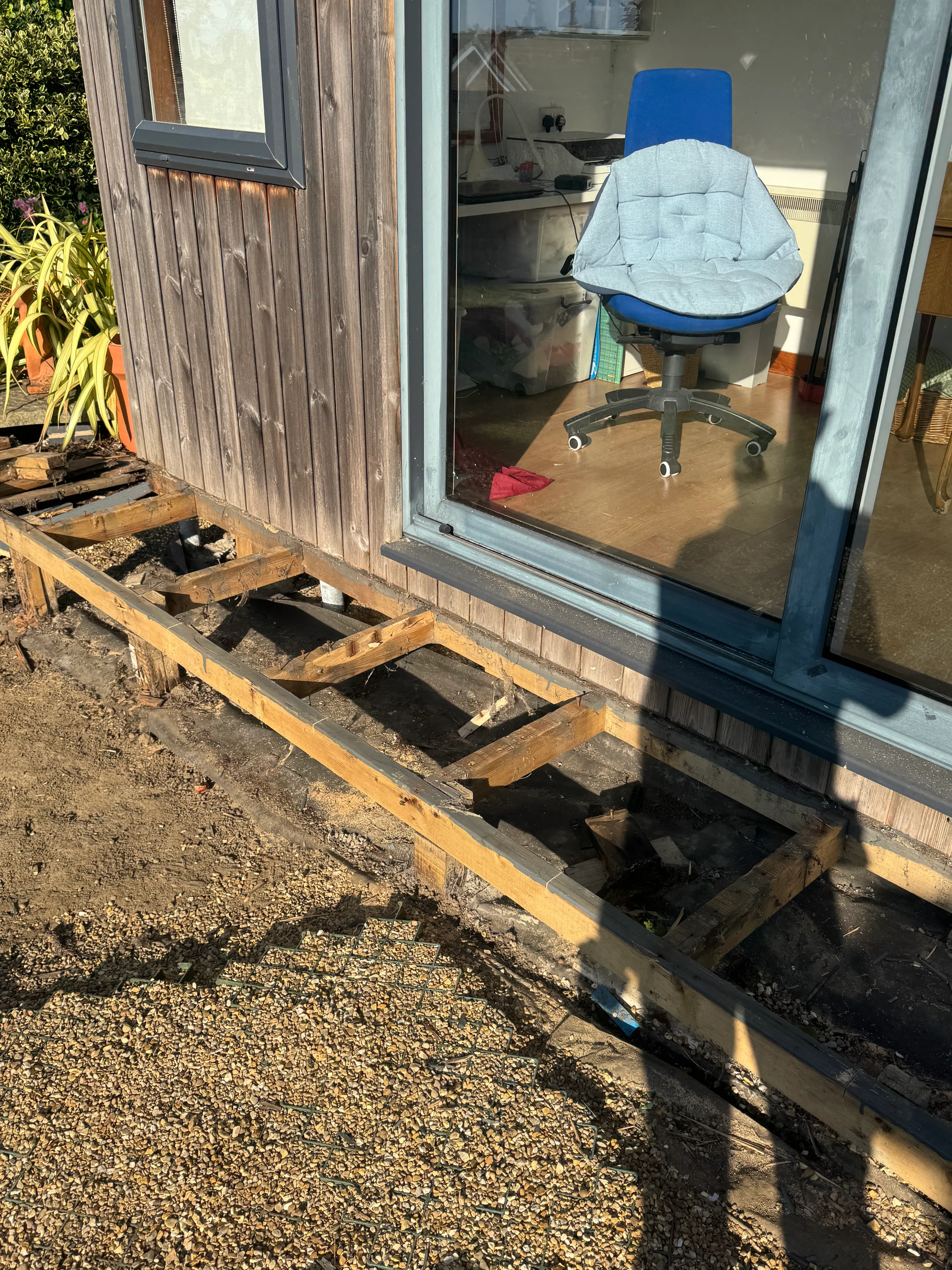 Old decking lifted, showing the rotted timber frame and bare ground underneath