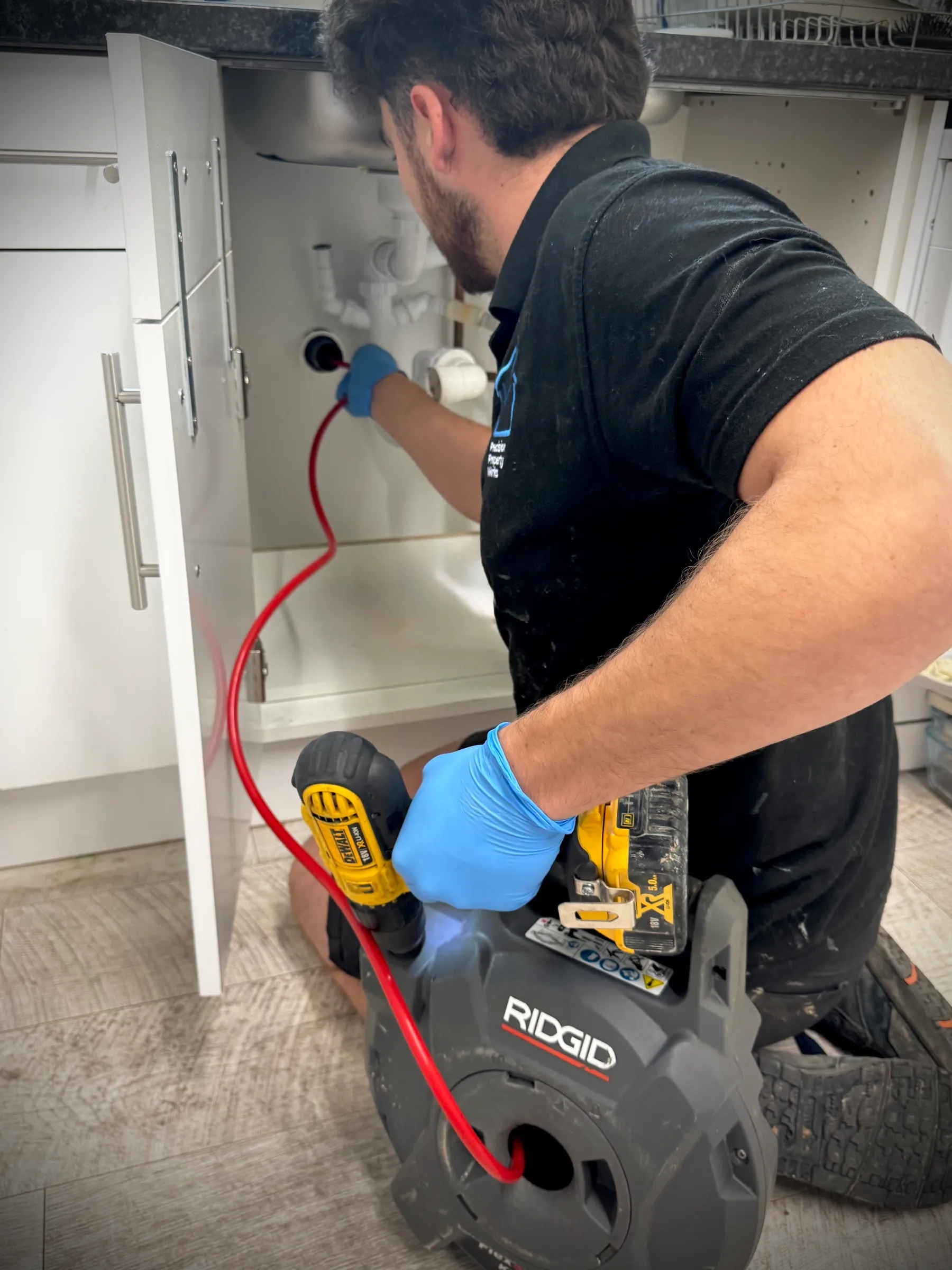 Feeding the flexible shaft of a RIDGID K9-12 machine into a kitchen waste pipe under the sink